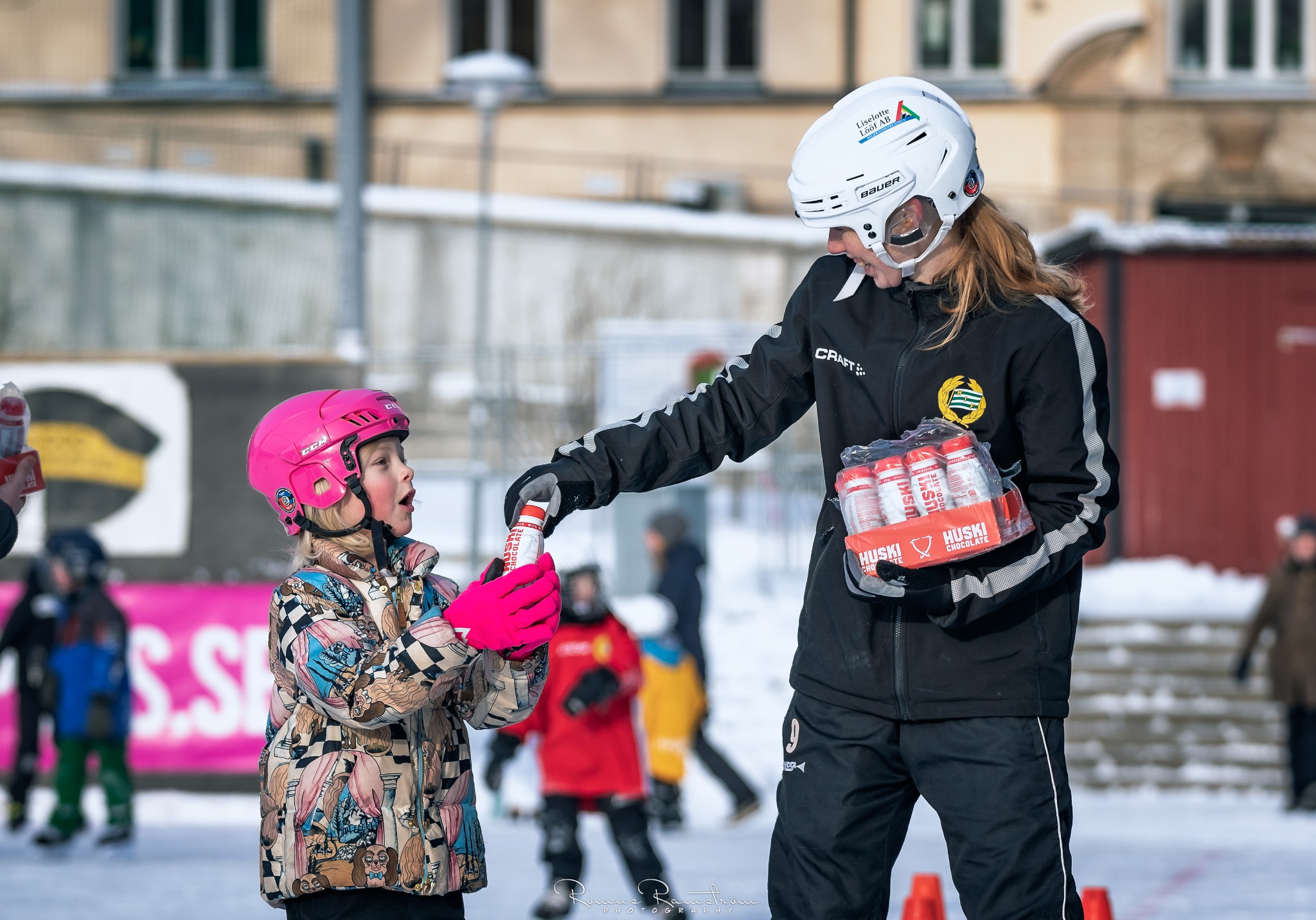 Ledare på isen räcker över en dryck till ett barn under träning.